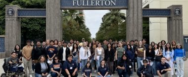 A large group of college students gather near the California State University Fullerton sign.