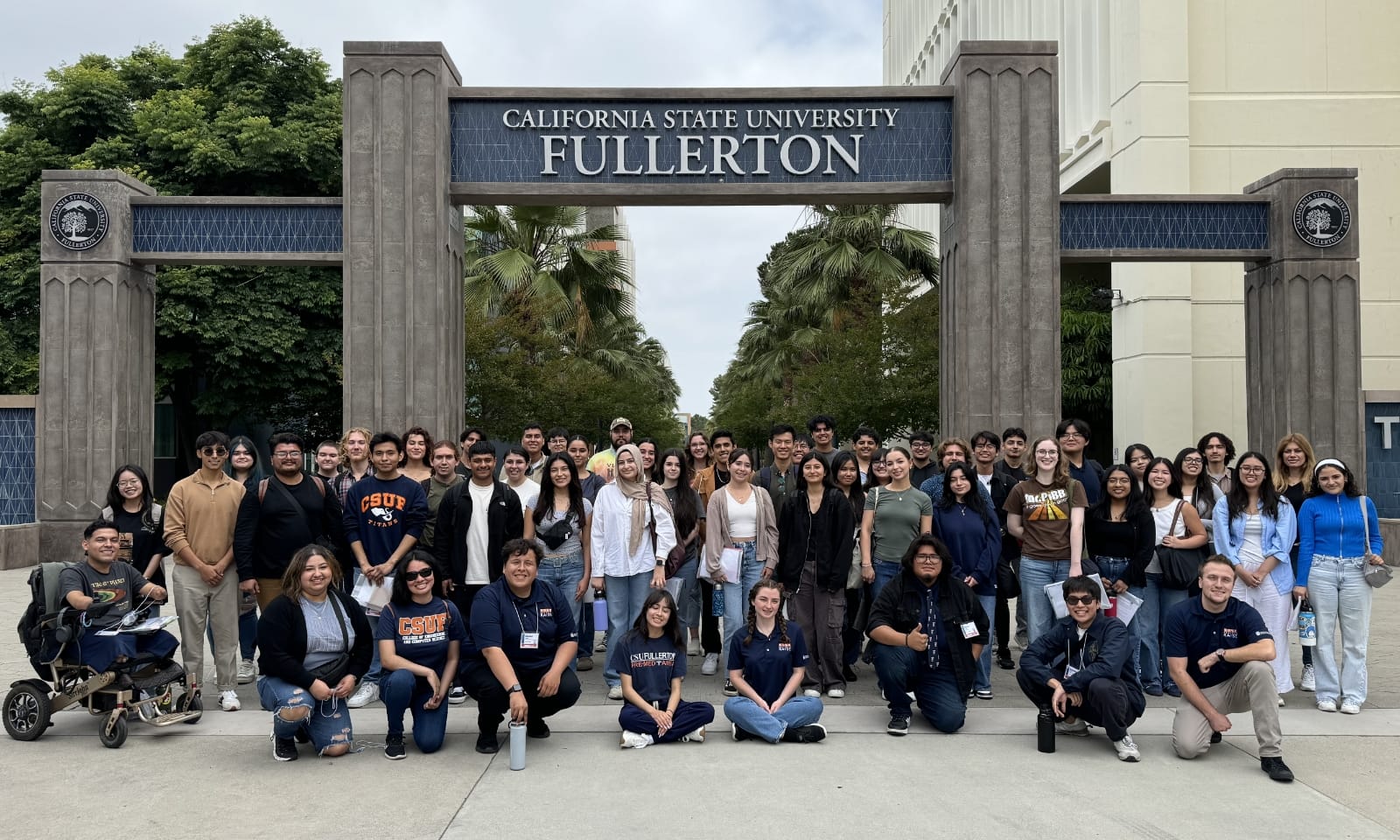 A large group of college students gather near the California State University Fullerton sign.