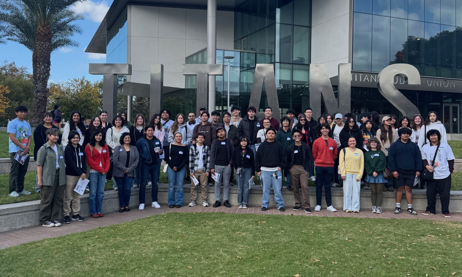 A large group of students stand near the Titans sign on CSUF’s campus.