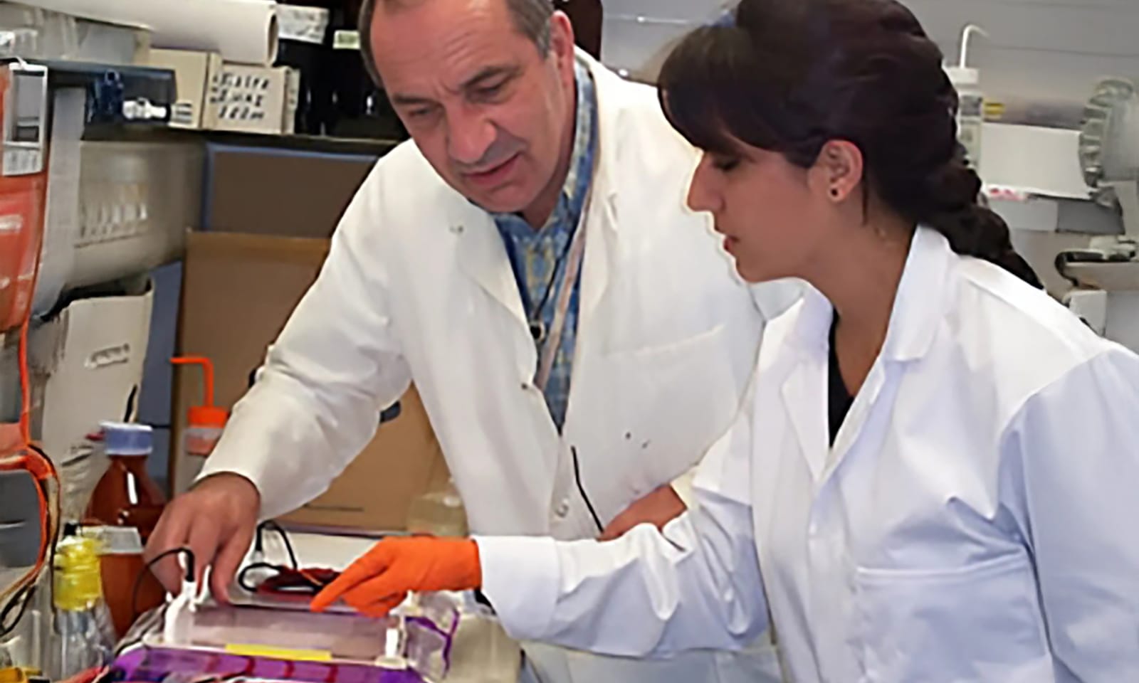 Two researchers in white coats work in a lab.