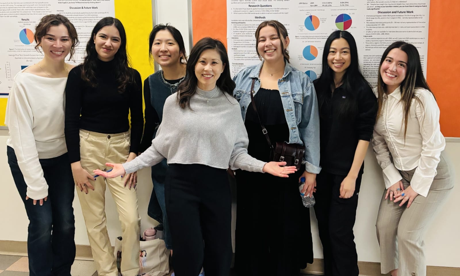 A smiling group of people pose in front of posters in a college hallway.