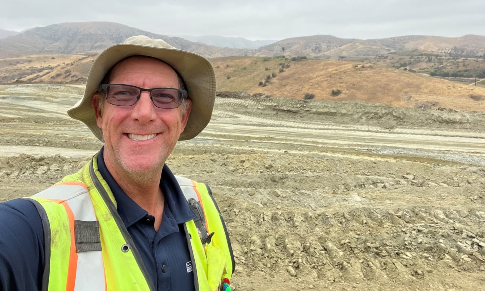 A man in hiking gear and a hat smiles at the camera.