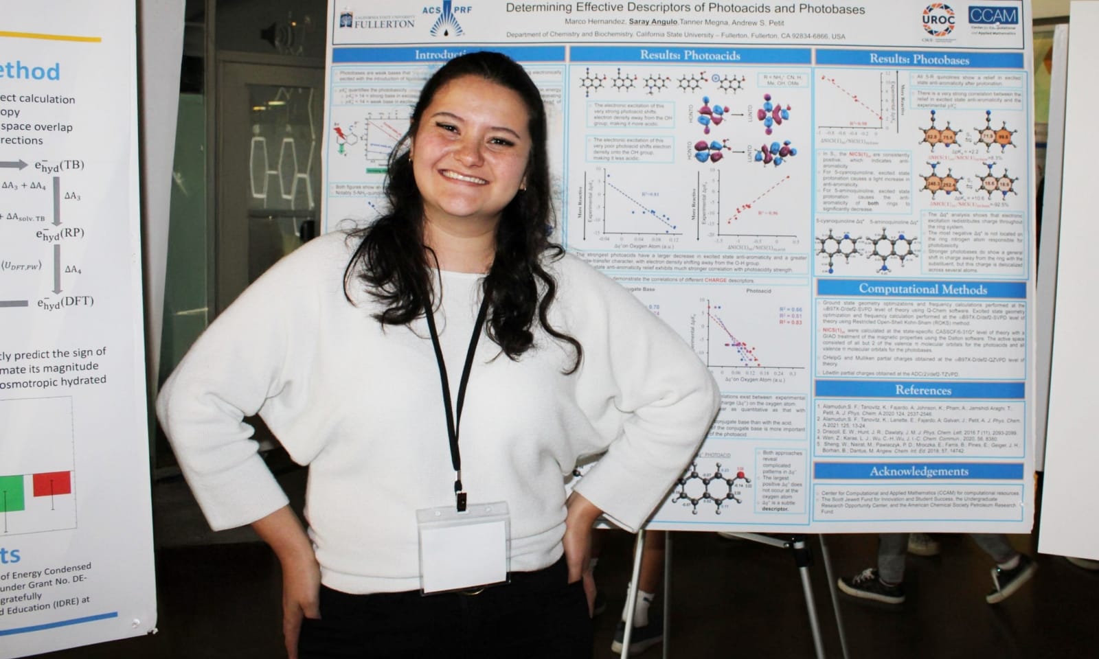 A chemistry student at Cal State Fullerton stands smiling in front of her research poster at a research symposium. She wears a white sweater and a name badge, showcasing her chemistry work.